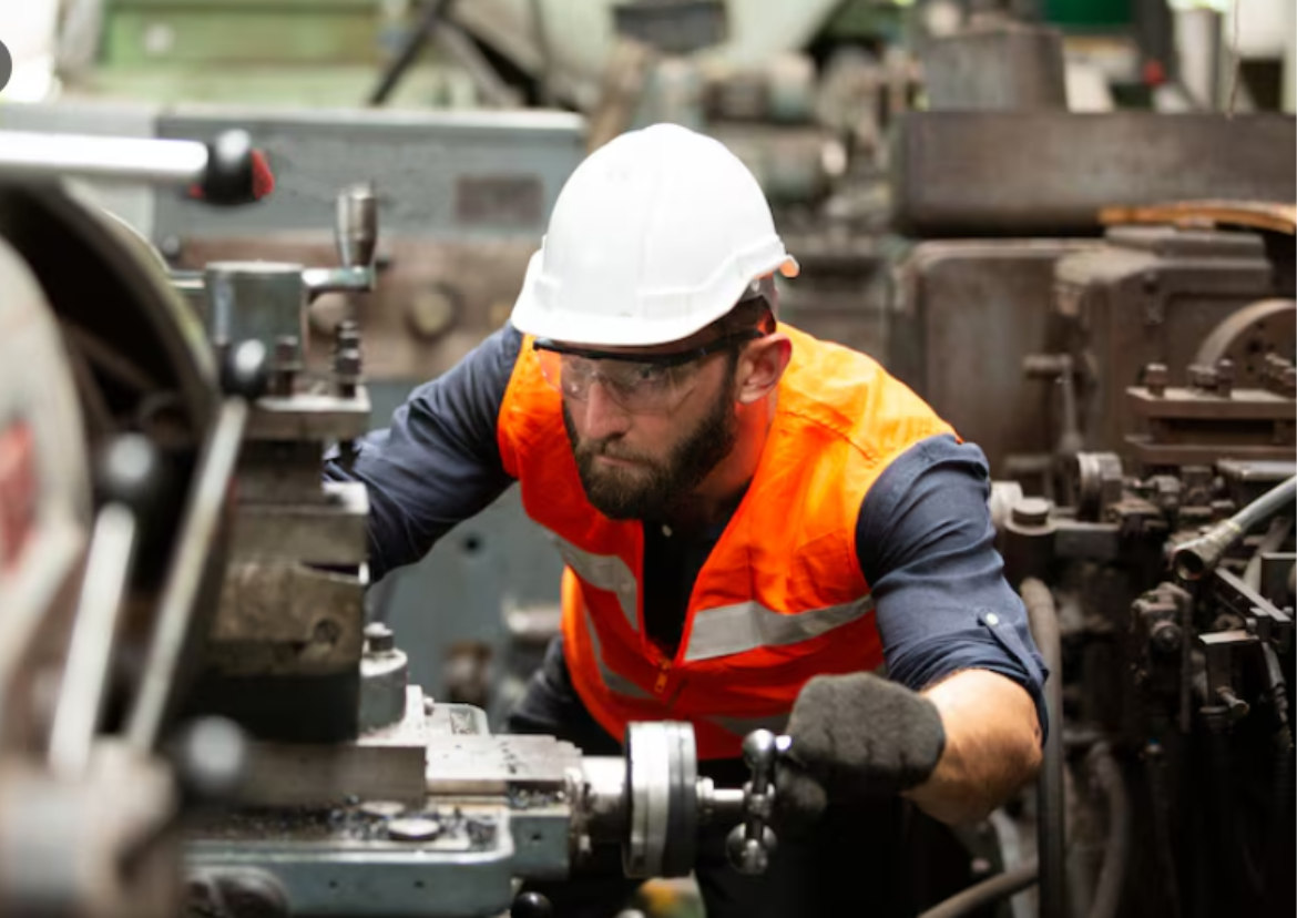 Trabalhador usando EPI operando máquina industrial conforme a NR 12 — serviços de segurança do trabalho da Prisma Engenharia em Fortaleza-CE.